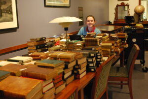 piles of old books on a table with a smiling college student